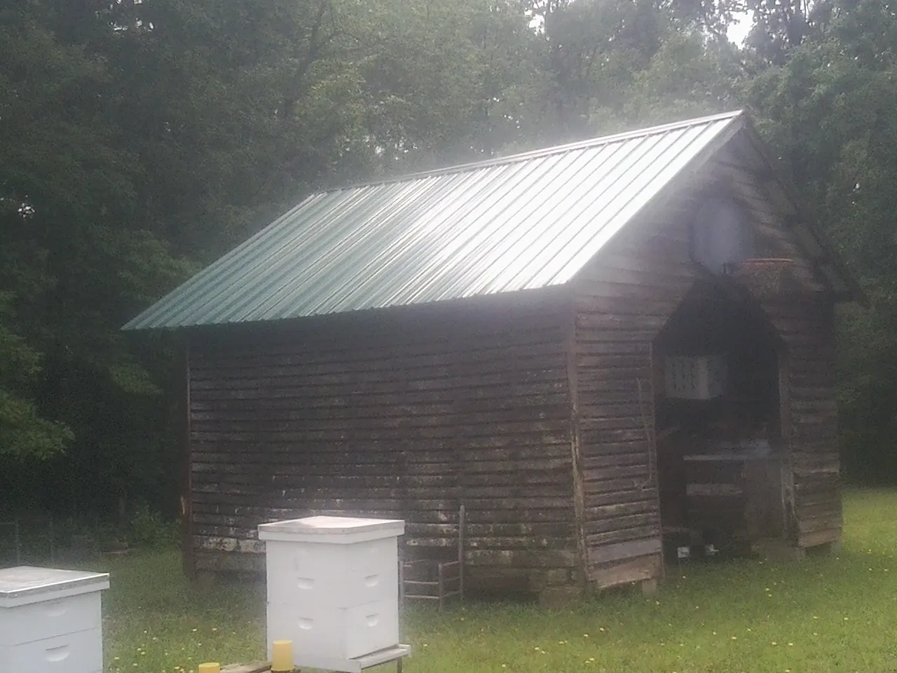 Green metal roof on a weathered barn beside stacked beehives in Madison